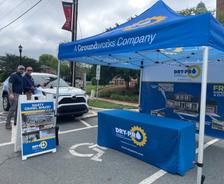 Two men stand by a DRY-PRO tent and display, promoting crawl space services at an outdoor event in a parking lot.