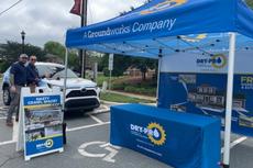 Two men stand by a DRY-PRO tent and display, promoting crawl space services at an outdoor event in a parking lot.