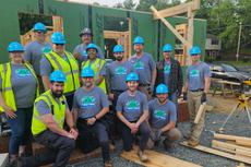 A group of construction workers in blue helmets pose together at a home building site.