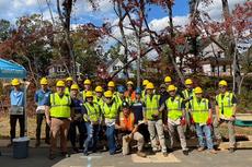 A group of people in safety vests and hard hats pose together outdoors at a construction site.
