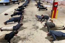 A group of people doing push-ups in rows inside a large industrial warehouse.