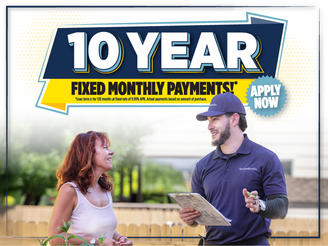 A worker talks with a smiling woman outdoors under a banner reading "10 Year Fixed Monthly Payments.