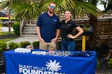 Two people stand behind a "Mount Valley Foundation Services" booth with sunglasses and items on the table.