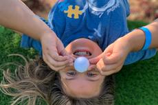 Child lying upside down on grass, holding a golf ball to their nose and smiling playfully.