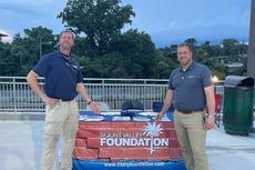 Two men stand by a Mount Valley Foundation Services table display outdoors in the evening.
