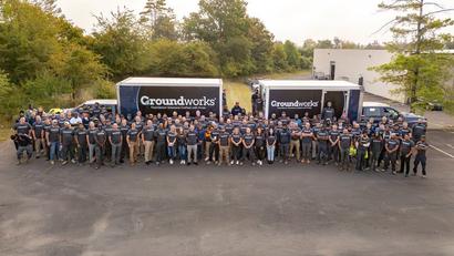Groundworks Team posing in matching shirts posing in front of two Groundworks trucks in a parking lot.