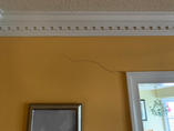 A visible crack runs diagonally across a yellow wall above a door and picture frame.