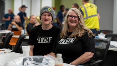 Two people smiling, sitting together at a table during an indoor event.