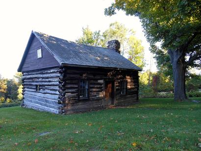 Adsit Log House, a historic log cabin in Willsboro Point, New York, with a stone chimney and weathered log exterior.