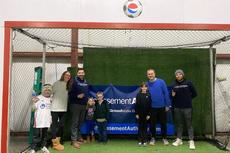 A group of people, including children, standing and posing inside an indoor soccer goal.