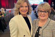 Two women smiling at a fashion event with a "HAUTE" sign in the background.