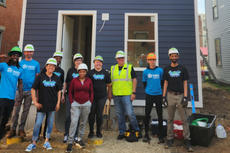 A group of volunteers in hard hats stand in front of a newly built house.