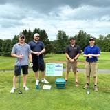 Groundworks Albany employees stand next to a company sponsorship sign at the annual "Dolly Day" Lazarou Memorial Golf Tournament