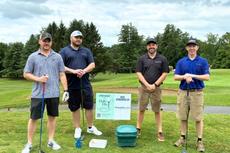 Groundworks Albany employees stand next to a company sponsorship sign at the annual "Dolly Day" Lazarou Memorial Golf Tournament