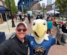 A man takes a selfie with a person in a bird mascot costume at an outdoor event in Cleveland.