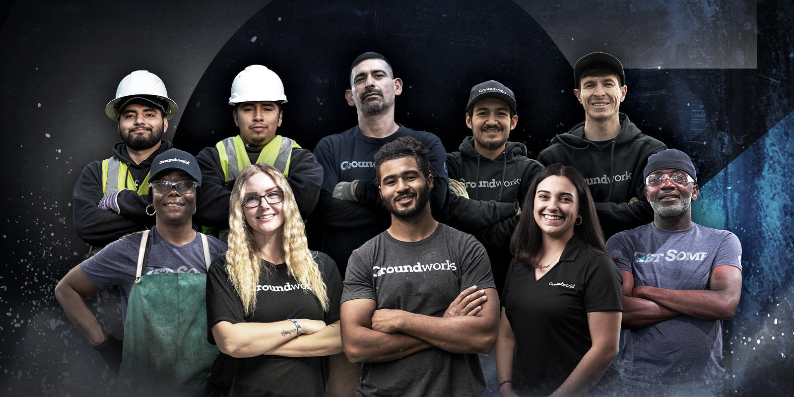 A diverse group of ten smiling workers pose together, some in uniforms and safety gear, against a dark, abstract background.
