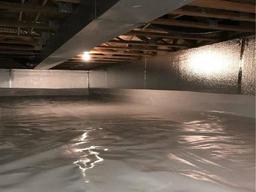 The crawl space, with reflective insulation and a vapor barrier on the floor, is softly illuminated by a single light bulb. Strategically placed crawl space vents ensure proper airflow and maintain an optimal environment.