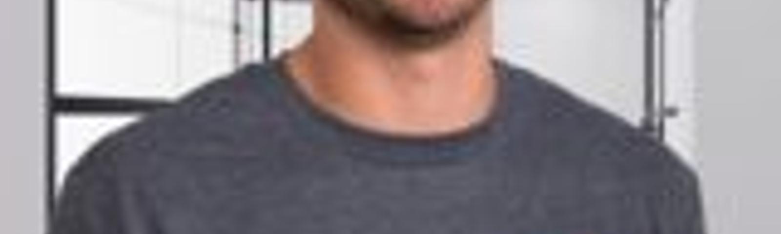 Smiling man in a grey t-shirt stands in a modern hallway with glass partitions.