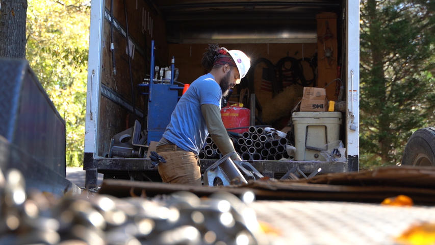 Person in blue shirt working with tools inside an open truck, surrounded by equipment and machinery parts.