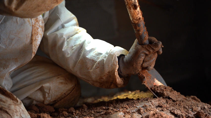 worker digging in crawl space with shovel