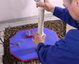 Person installing a white PVC pipe into a blue sump pump cover surrounded by gravel.