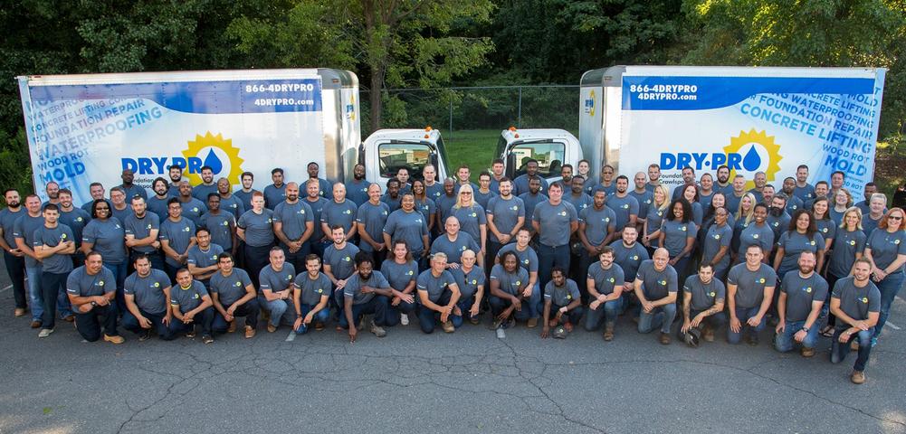 A large group of people in matching shirts gather in front of two company trucks.