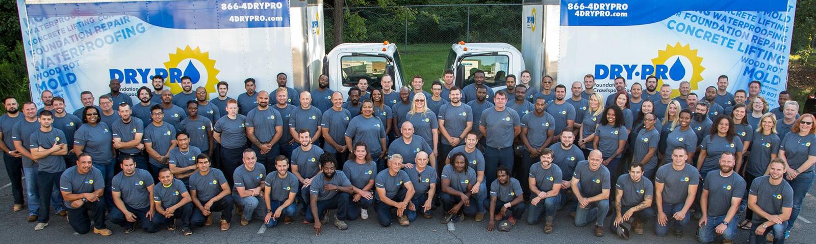 A large group of people in matching shirts gather in front of two company trucks.