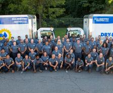A large group of people in matching shirts gather in front of two company trucks.
