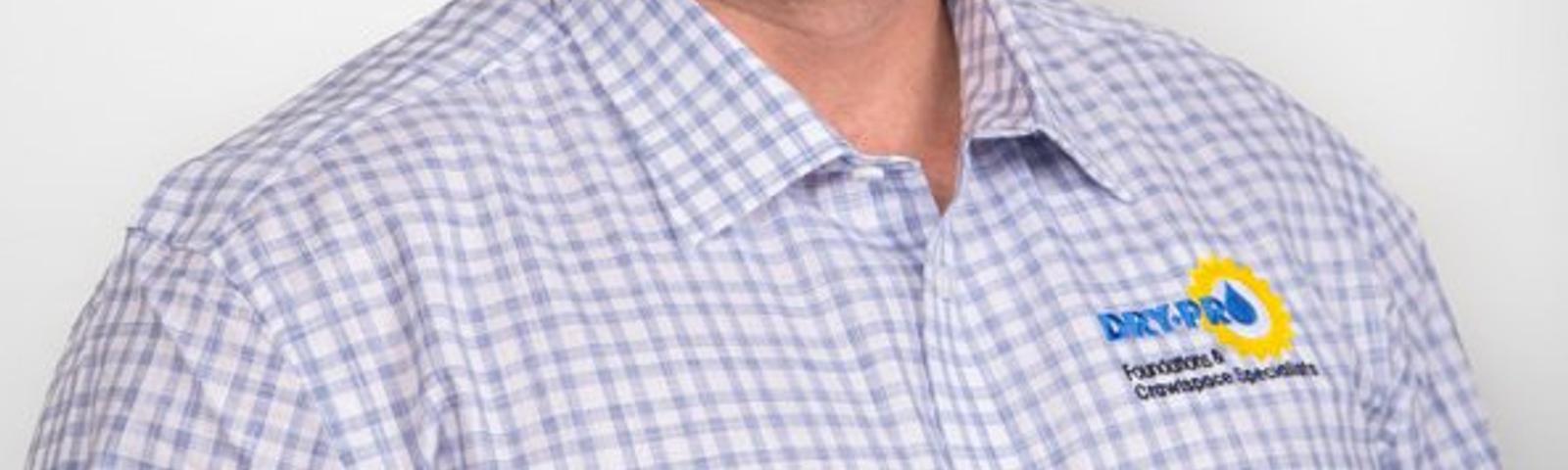 Smiling person in a checkered shirt stands against a plain background.