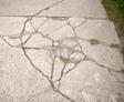 Cracked concrete sidewalk with grass on the right side.