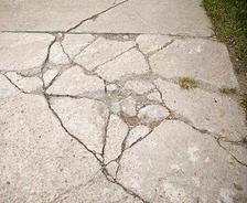 Cracked concrete sidewalk with grass on the right side.