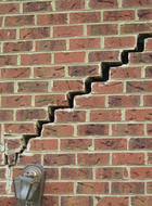 A brick wall with a large, jagged crack running diagonally hints at potential foundation issues, while a light fixture rests at the bottom.