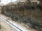 Deep excavation site with exposed earth layers, vertical rebar rods in place along the trench edges.