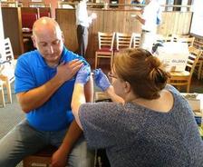 A man in a blue shirt receives a vaccination in a restaurant setting.