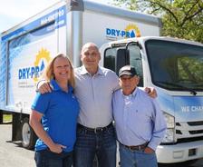 Three people stand smiling in front of a Dry Pro truck with the slogan "We Change Lives" on it.