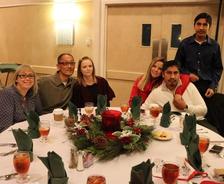 Group of six people seated around a decorated round table with drinks and holiday centerpieces.