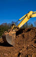 Yellow excavator digging in a dirt mound with a clear blue sky background.