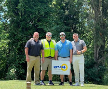 Four men posing outdoors with a "Dry-Pro" sign, surrounded by lush trees.