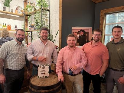 Five men standing together in a bar, casually dressed, smiling at the camera.