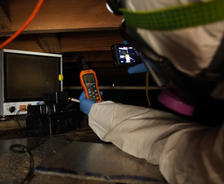 Person in protective gear uses inspection tools in a dimly lit crawl space, monitoring crawl space humidity and equipment readings.