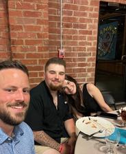 Three people smiling at a restaurant table with empty plates and glasses in front of a brick wall.