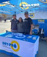 Three Dry Pro Foundation and Crawlspace Specialists crew members standing smiling behind brand sponsorship booth underneath canopy at Lincoln County Apple Festival