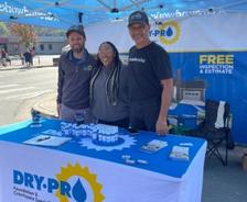 Three Dry Pro Foundation and Crawlspace Specialists crew members standing smiling behind brand sponsorship booth underneath canopy at Lincoln County Apple Festival