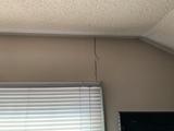 A vertical crack in drywall runs from the ceiling down the beige wall above window blinds.