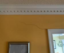 A visible crack in drywall runs across a yellow wall above a framed picture and near a white door frame.