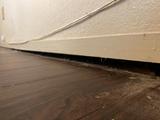Gap between a wooden floor and baseboard along a wall with visible wiring, often a sign of sagging floors.