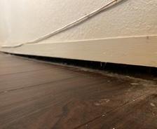 Gap between a wooden floor and baseboard along a wall with visible wiring, often a sign of sagging floors.