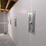Metal anchor plates are bolted into a white basement wall with exposed beams visible at the ceiling.