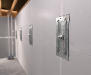 Metal anchor plates are bolted into a white basement wall with exposed beams visible at the ceiling.