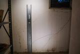 Metal support beam leaning against a cracked basement wall under a small window with visible exterior light.